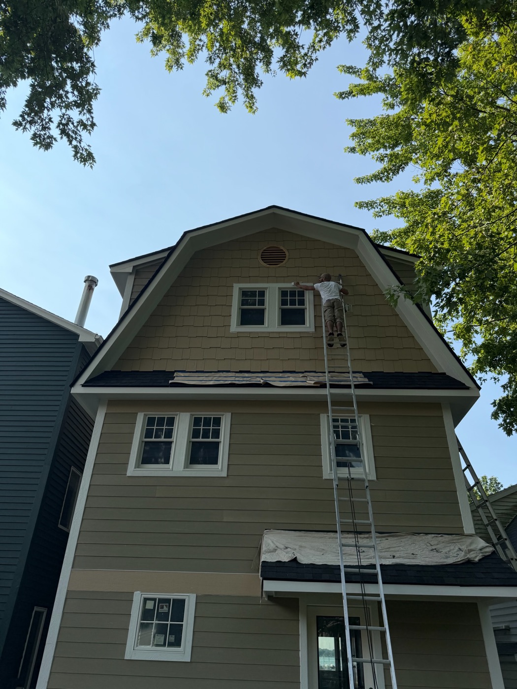 A Pointe Painting Company painter working from a ladder on a shingled gambrel exterior