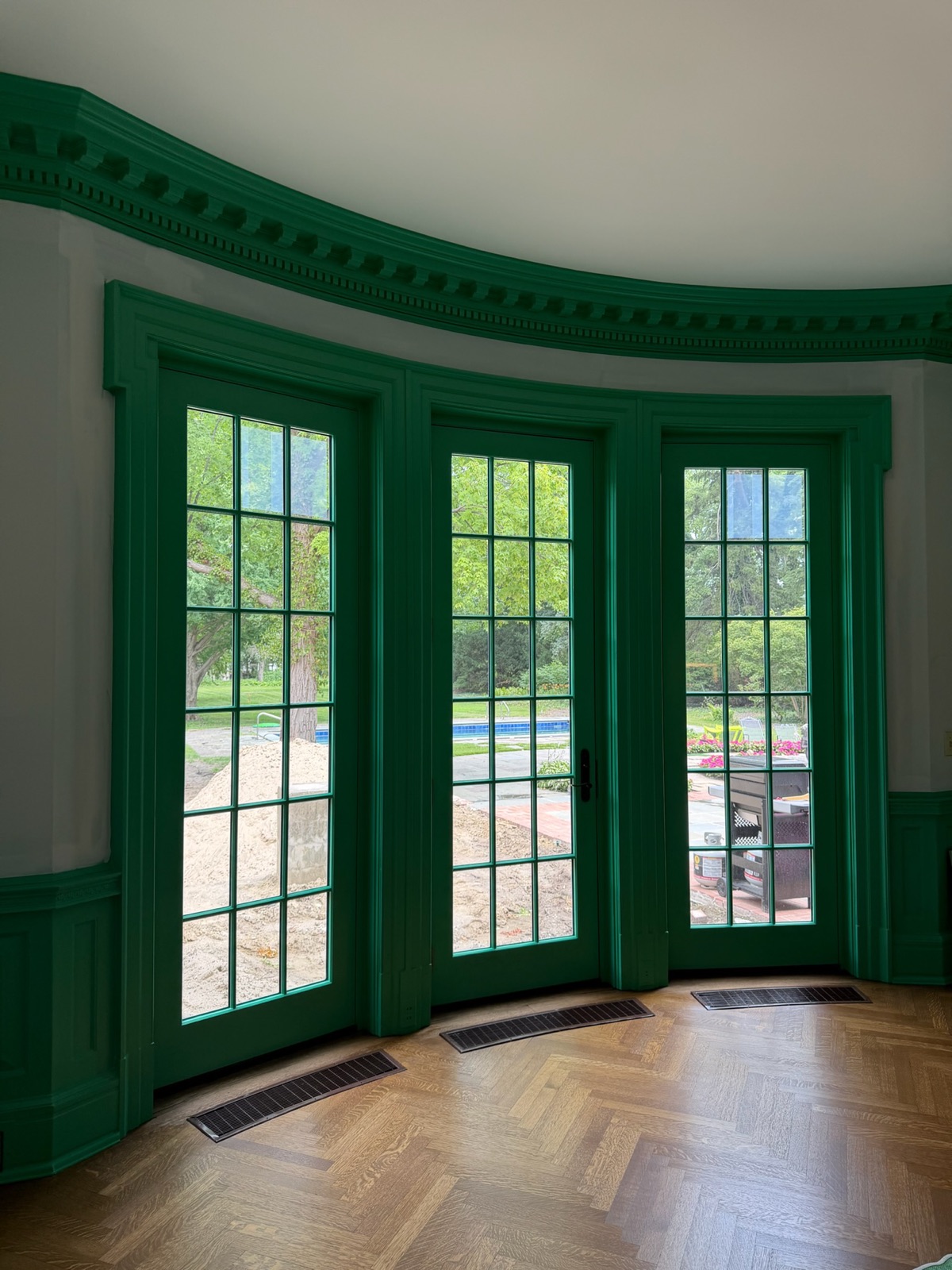 Emerald-painted French doors and dentil crown in a curved room with herringbone floors