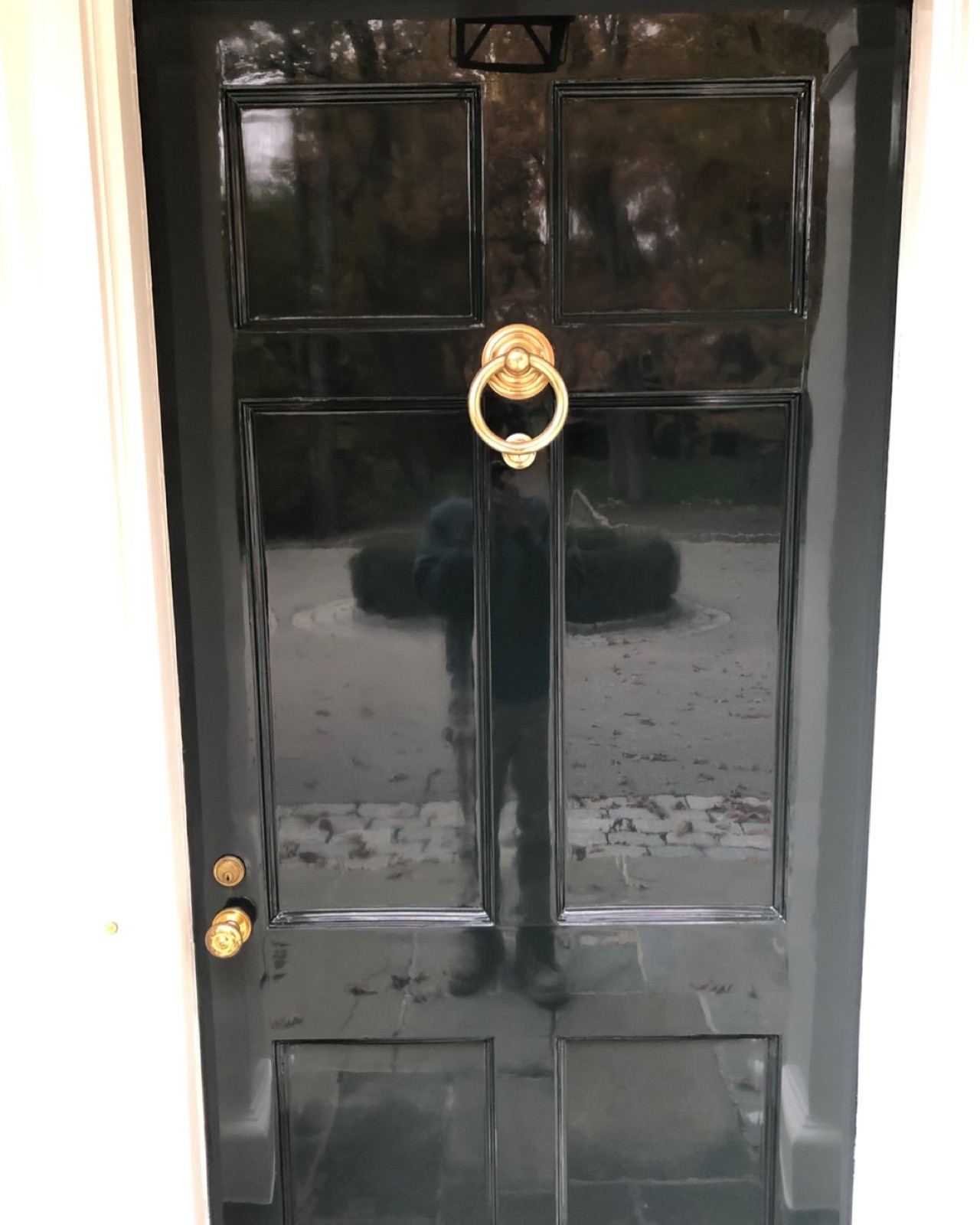 Mirror-gloss front door in deep green-black with a polished brass knocker