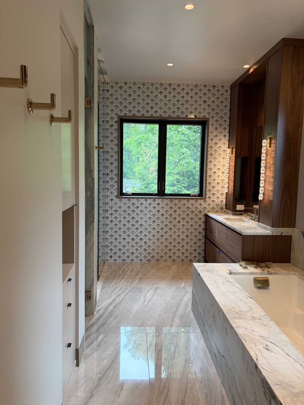 Primary bathroom with marble surfaces, fan-pattern tile and a walnut vanity wall