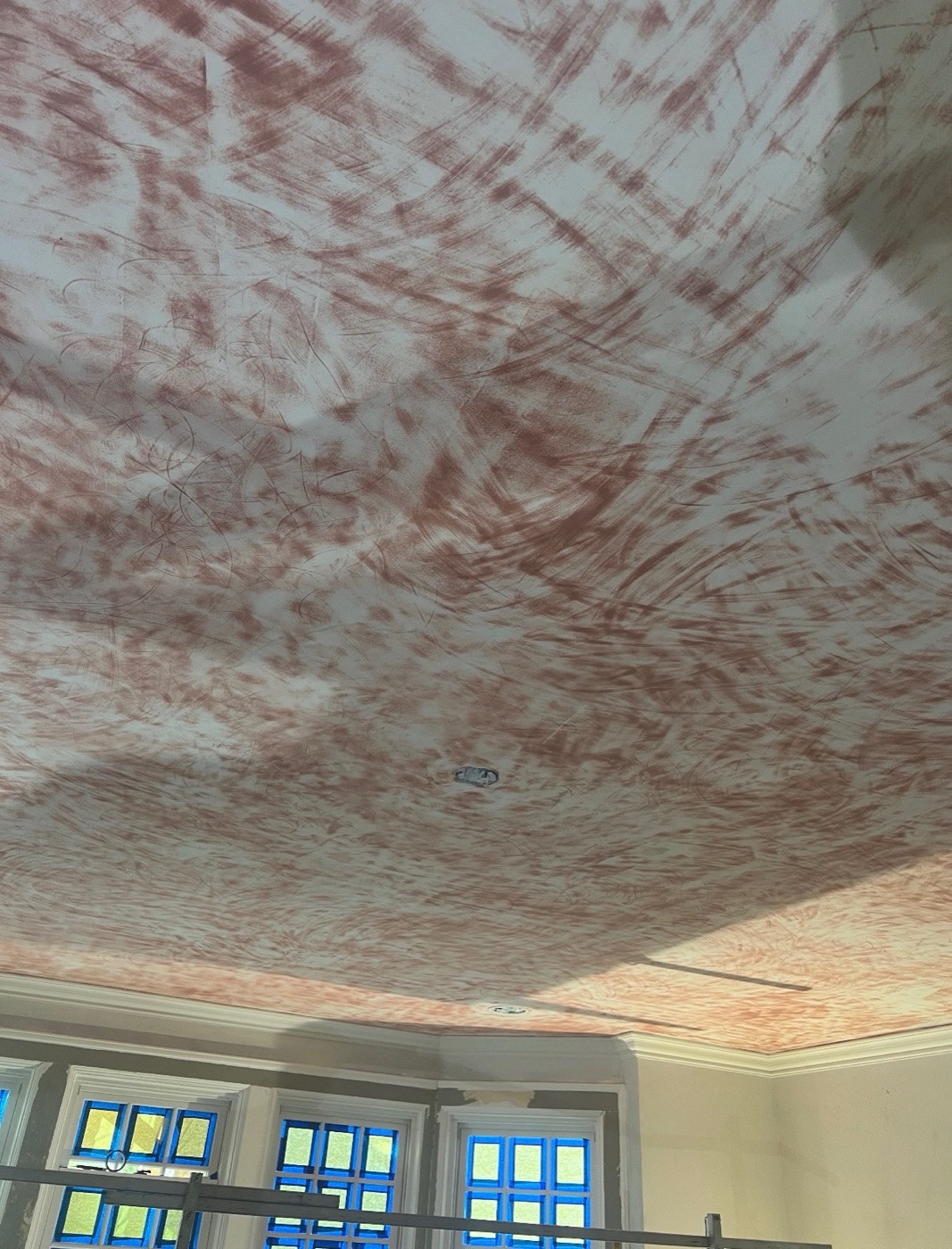 Hand-applied strie glaze in progress across a ceiling, rust red over white